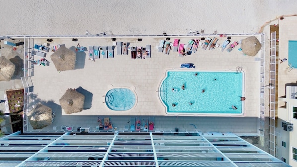 A rooftop pool area with multiple swimming pools, lounge chairs, and umbrellas.
