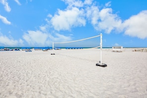 A beach volleyball court with a net, blue chairs, and a white structure in the background.