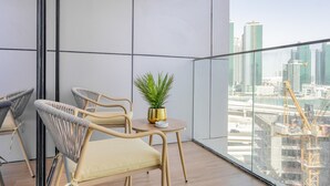 A balcony with wicker chairs, a small table with a potted plant, and a city view.