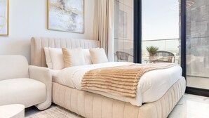 A modern bedroom with a large bed, a chair, and a balcony with a view.