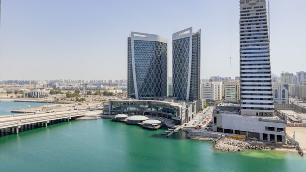 A modern building complex with a waterfront view, featuring two prominent towers and a large building with a unique facade.