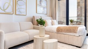 A modern bedroom with a sofa, a bed, and a round wooden table with a vase.