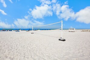 Una cancha de voleibol de playa con una red, sillas azules y una estructura blanca al fondo.