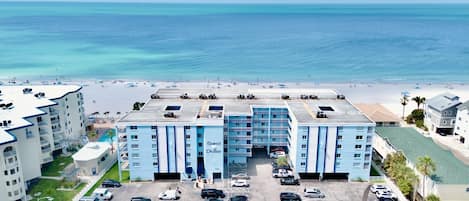 A hotel with a pool, parking lot, and beach view.