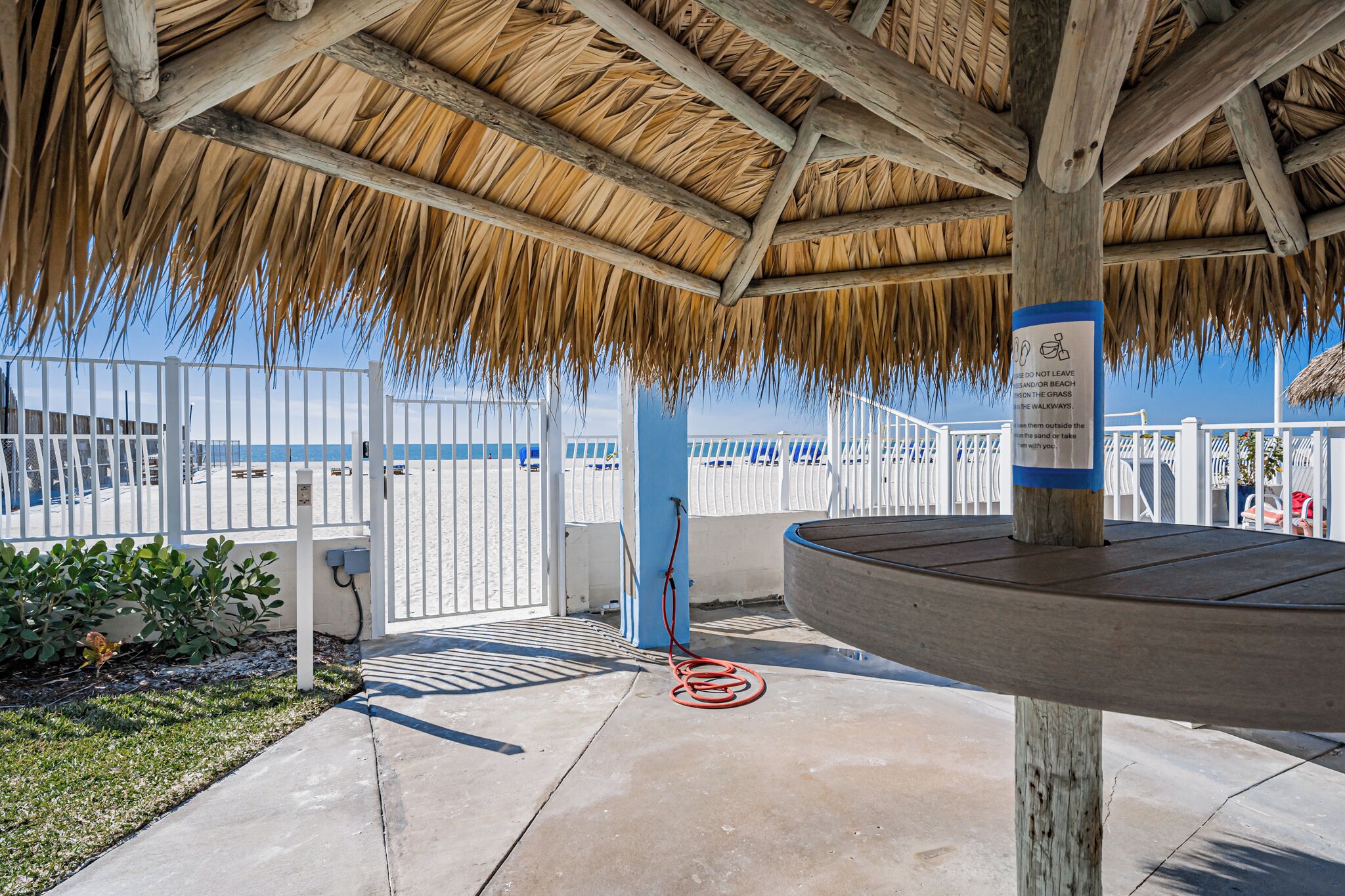A covered outdoor area with a thatched roof, a white fence, and a blue pillar with a sign.