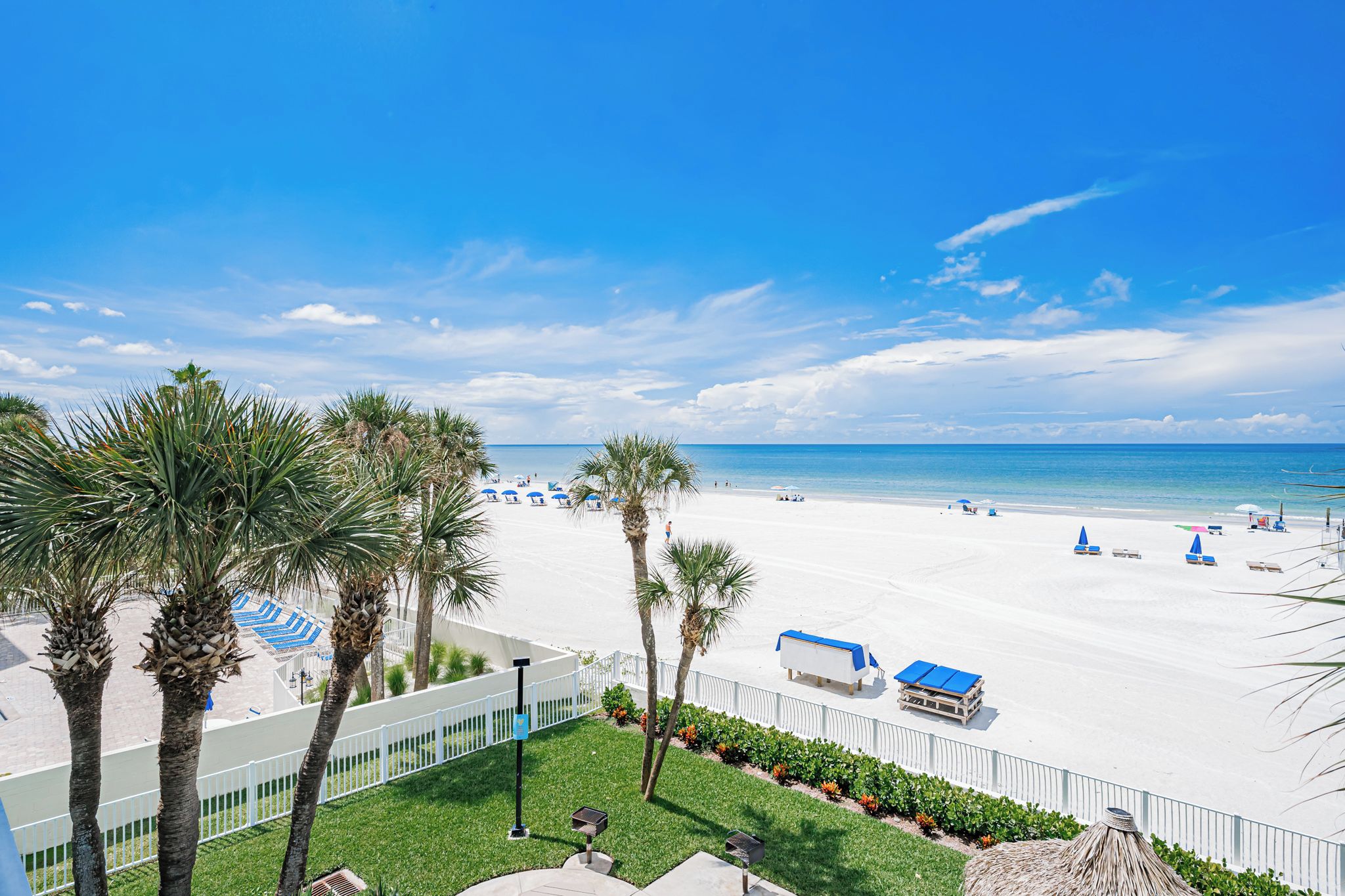 Een strand met wit zand, palmbomen en blauwe parasols.