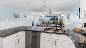 A modern kitchen with white cabinetry, granite countertops, and pendant lighting. - Sand Dollar 203 is a Silver Tier 3-bedroom 2 bath Gulf Front Condo (Indian Shores)