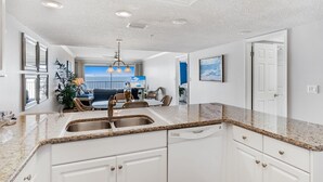 A modern kitchen with granite countertops, white cabinetry, and a built-in dishwasher. - Light and Airy Gulf Front Condo w/ Balcony - SD205 (Indian Shores)