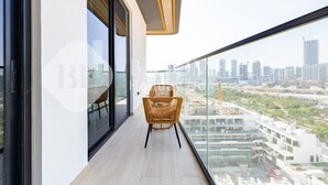 Een balkon met een rieten stoel, een glazen deur en uitzicht over de stad.