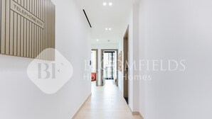 Een moderne gang met een bordje voor een telefooncel, die leidt naar een lichte kamer met een deur aan het einde.