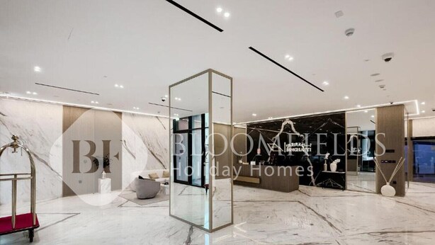 Een ruime, moderne hotel lobby met een marmeren vloer, een glazen scheiding en een zithoek met een bank en een bijzettafeltje.