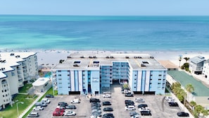 A hotel with a pool, parking lot, and beach view.