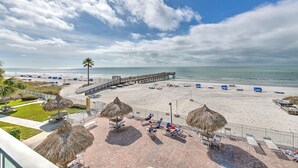 A beach with a wooden pier, lounge chairs, and thatched umbrellas.