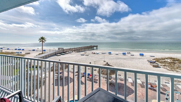 A beach view from a balcony with a wooden pier, beach chairs, and umbrellas.
