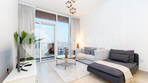 A modern living room with a sofa, a coffee table, and a TV on a white cabinet. - Bloomfields Spacious 1BR Bloom Tower (Dubai)