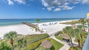 A beach view with a pier, palm trees, and a pool area.