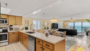 A modern kitchen with wooden cabinets, a central island, and a dining area with a view.