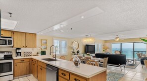 A modern kitchen with wooden cabinets, a central island, and a dining area with a view.