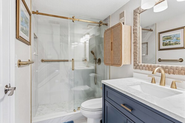 A bathroom with a glass-enclosed shower, a white toilet, a vanity with a sink, and a mirror with a picture frame.