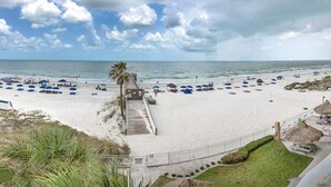 A beach with a wooden walkway leading to the water, umbrellas, and beach chairs. - Huge 3rd Floor Gulf Front Condo w/ Balcony SD304 (Indian Shores)