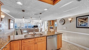 Cocina con encimeras de granito, gabinetes de madera y electrodomésticos de acero inoxidable, además de iluminación colgante.