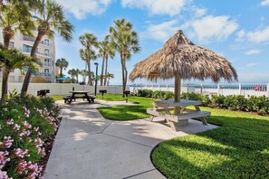 Ein Resorthotel mit einem Reetdachschirmchen, Picknicktischen und einem Weg zum Strand.