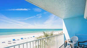 Ein Balkon mit Blick auf einen Strand, weißem Geländer und einem Tisch mit Stühlen.