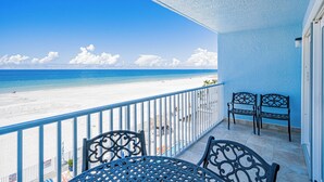 A balcony with a view of a beach and ocean. There are two chairs and a table.