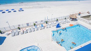 A pool area with lounge chairs and a hot tub, surrounded by a white sandy beach.