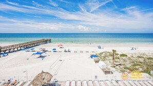 A beach with a pier, beach umbrellas, lounge chairs, and a thatched hut. - Spacious Gulf Front Condo w/ Big Balcony - SD310 (Indian Shores)