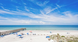 A beach with a wooden pier, beach umbrellas, and lounge chairs. - Spacious Gulf Front Condo w/ Big Balcony - SD310 (Indian Shores)