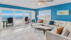 A spacious living room with a large window overlooking the ocean, a ceiling fan, and a cozy seating area with a sofa and chairs.