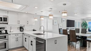 Una cocina moderna con armarios blancos, electrodomésticos de acero inoxidable e iluminación colgante.
