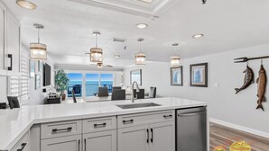 Cocina moderna con una isla grande, iluminación colgante y vistas al exterior.