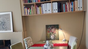 Un comedor con una mesa, sillas, una estantería, un cuadro y una lámpara.