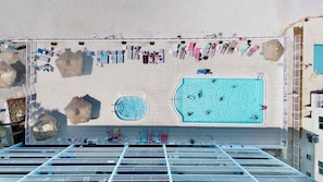 Un espace piscine sur le toit, comprenant plusieurs piscines, des chaises longues et des parasols.