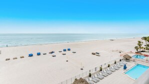 A beach view with a pool area, lounge chairs, and umbrellas.