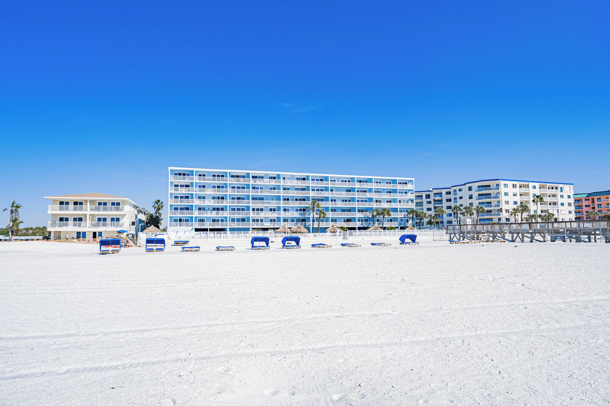Ett hotell vid stranden med flera våningar, en sandstrand framför och en klarblå himmel.