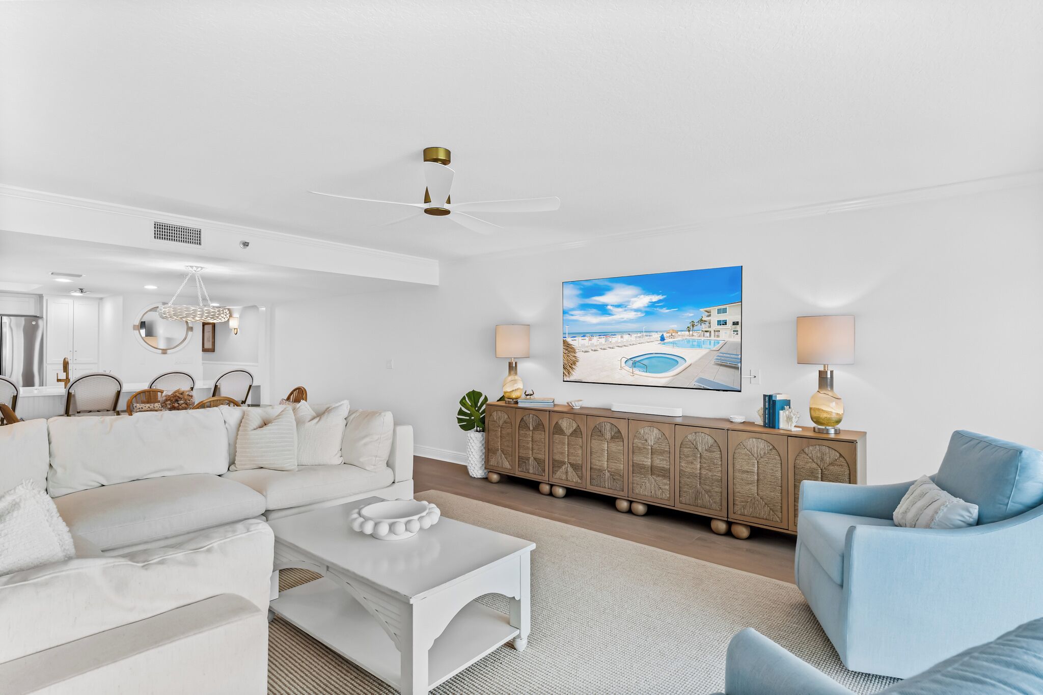Una sala de estar moderna con un sofá blanco, un sillón azul, una mesa de centro y un mueble de madera con adornos.