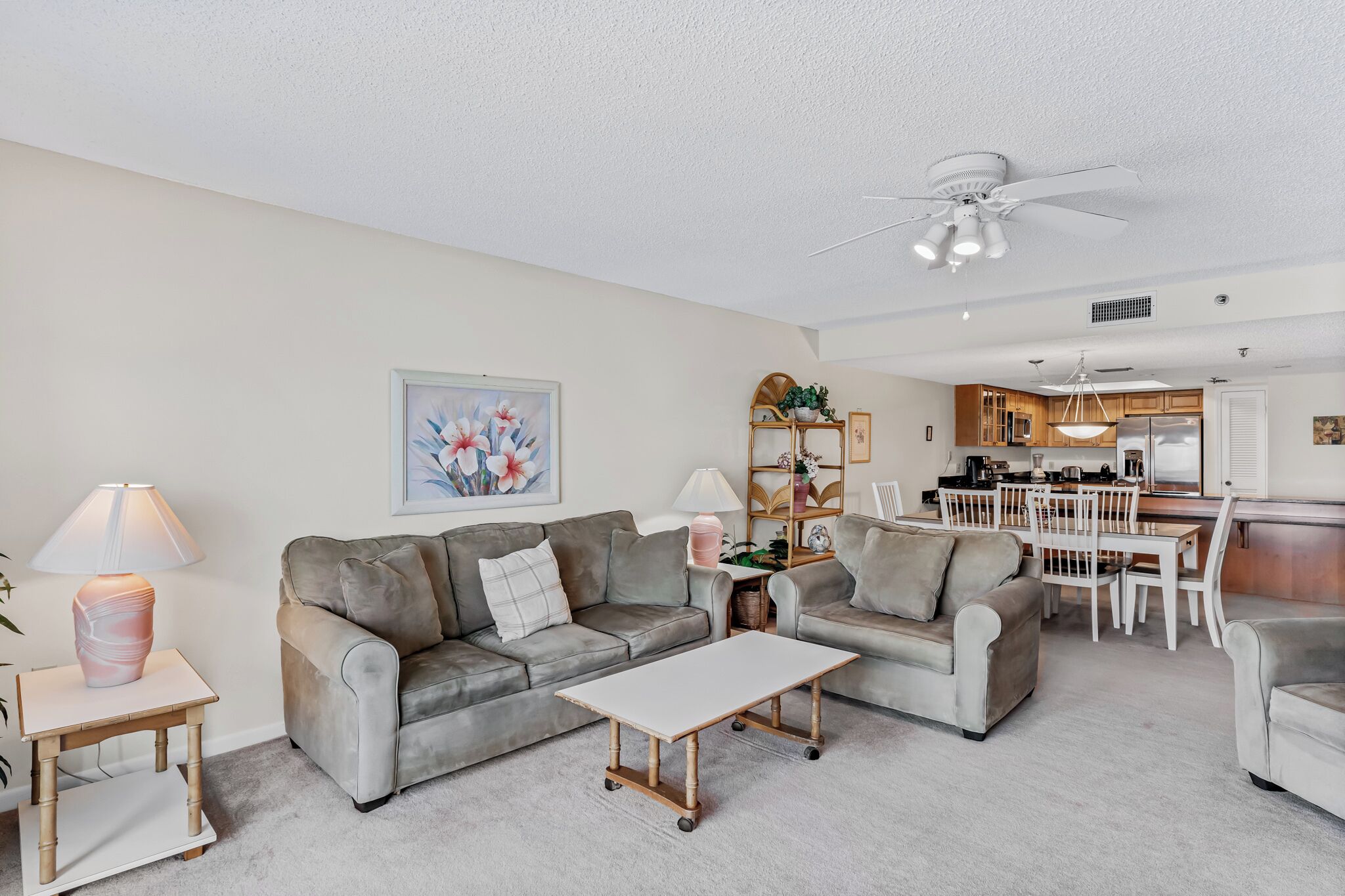 A modern living room with a grey sofa, a white coffee table, and a dining area with a kitchen in the background.