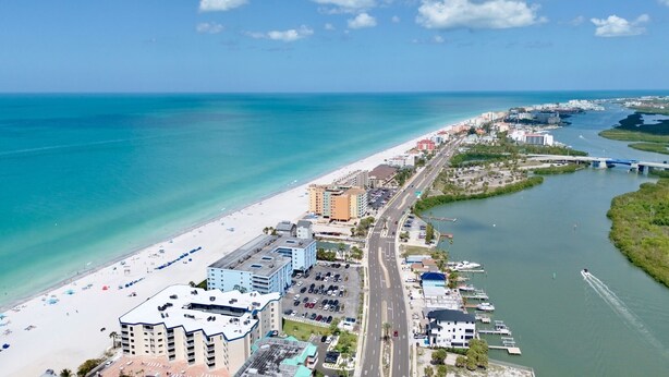 Un paisaje urbano costero con playa, puerto deportivo y puente.