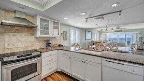 A modern kitchen with white cabinets, a stainless steel range hood, and a granite countertop.