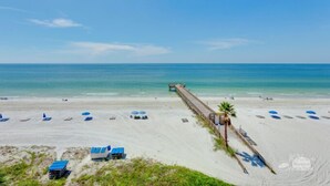 A beach with a pier extending into the ocean, beach chairs, and umbrellas.