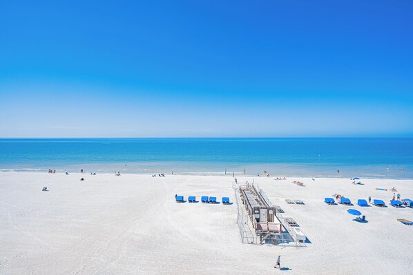 A beach with clear blue water, a sandy shore, and several blue umbrellas.