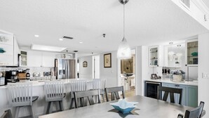 Una cocina moderna con muebles blancos, un comedor con mesa y sillas, y un refrigerador visible.