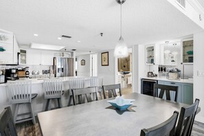 A modern kitchen with white cabinetry, a dining area with a table and chairs, and a visible refrigerator.