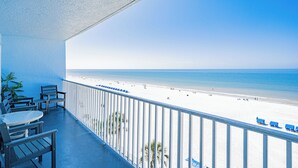 Un balcón con vista a la playa, una mesa y sillas.