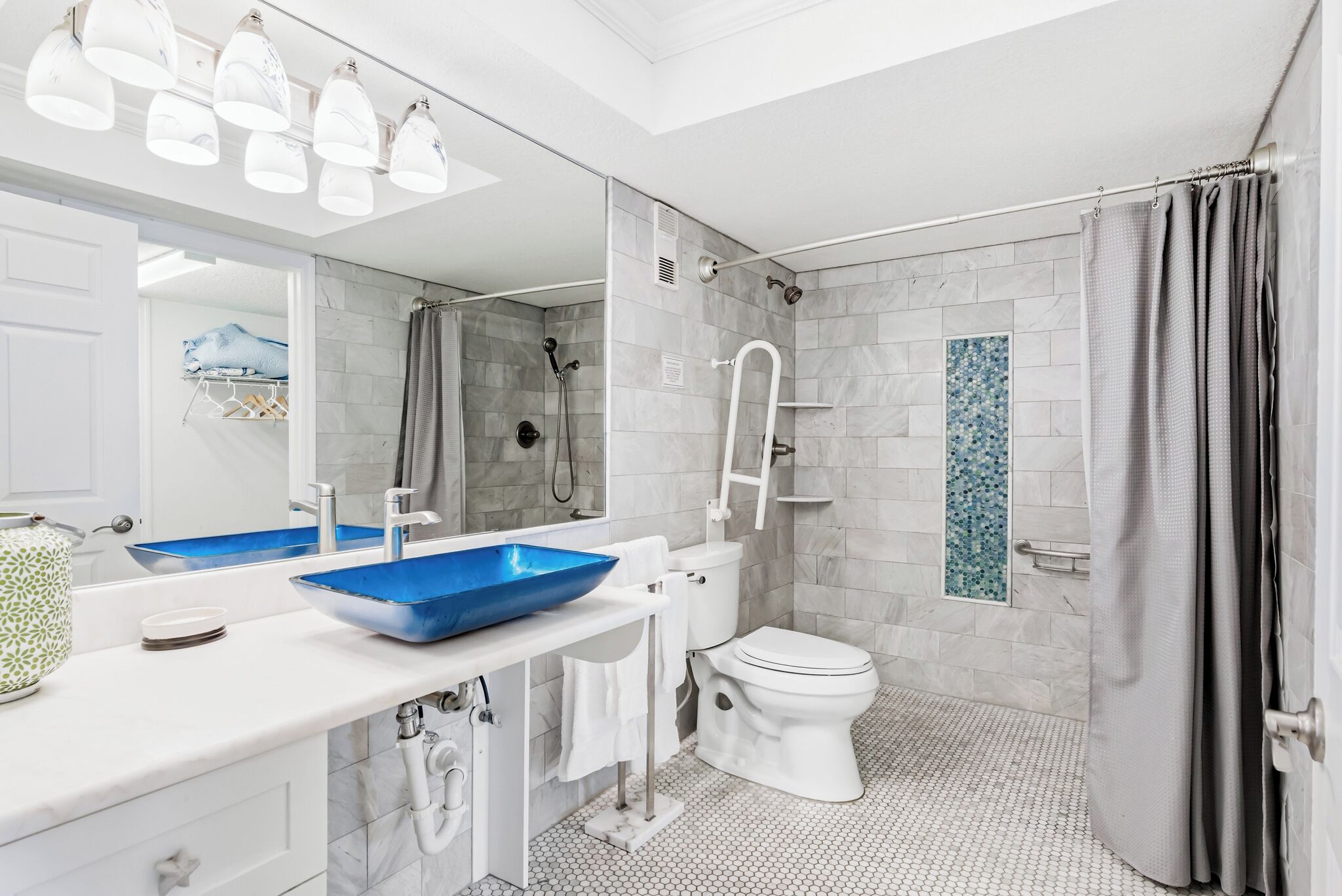 Un baño moderno con lavamanos blanco, lavabo azul, inodoro blanco y zona de ducha.