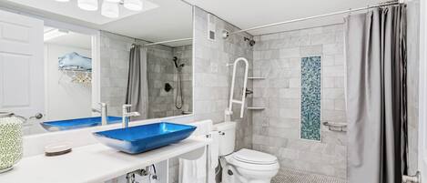 Un baño moderno con lavamanos blanco, lavabo azul, inodoro blanco y zona de ducha.