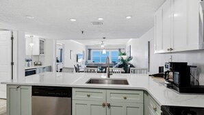 Una cocina moderna con armarios blancos, una isla central, electrodomésticos de acero inoxidable y vista al área de comedor.